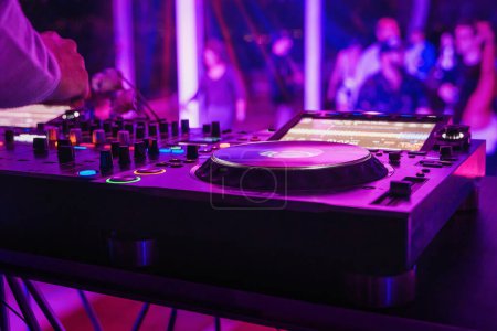 Téléchargez les photos : Gros plan d'une cabine de DJ dans une boîte de nuit, en mettant l'accent sur l'une des platines tournantes et l'éclairage coloré de la piste de danse - en image libre de droit