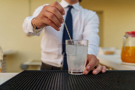 Téléchargez les photos : Un barman prépare un délicieux cocktail à l'aide d'un outil de mélange. L'accent est mis sur le verre et les techniques habiles du barman - section médiane - en image libre de droit