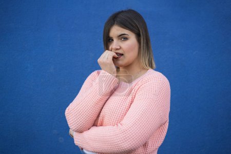 Photo for Young Caucasian plus-size woman biting her nails while looking at the camera with a demure expression. Concept of body shaming and nail-biting - Royalty Free Image
