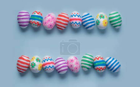 Foto de Coloridos huevos de Pascua decorados a mano sobre un fondo azul claro, dispuestos en dos filas horizontales con espacio de copia para un mensaje de Pascua personalizado. Utilizar como fondo para una pancarta o tarjeta de Pascua - Imagen libre de derechos