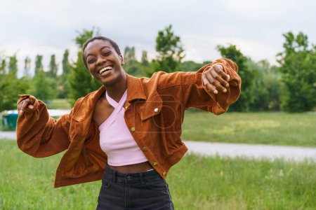 Foto de Una joven afroamericana con el pelo corto es vista bailando y riendo en un parque público durante la primavera - una chica negra vistiendo ropa casual, exudando alegría, vivacidad y juventud - Imagen libre de derechos