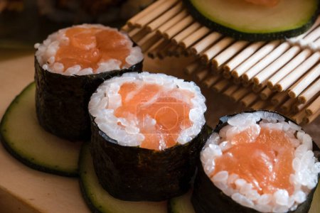 Téléchargez les photos : Gros plan de délicieux rouleaux de sushis au saumon placés sur des tranches d'avocat, entourés d'avocats supplémentaires et d'une présentation artistique en bambou. - en image libre de droit