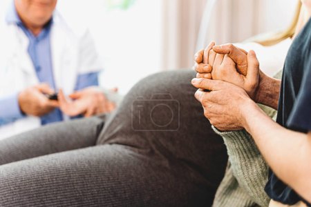 Photo for Unrecognizable lesbian couple at a gynecology appointment. Detail on their hands holding each other, and blurred doctor in the background - Royalty Free Image