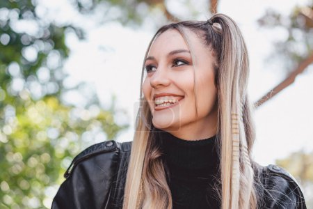 Photo for A stunning young woman with blonde and braided hair is captured outdoors on a sunny day. The photo features a shallow depth of field, with blurred trees in the background. - Royalty Free Image