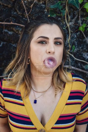 Téléchargez les photos : Jeune femme caucasienne soufflant chewing-gum dans une forme de ballon - Moment ludique et insouciant à l'extérieur - en image libre de droit