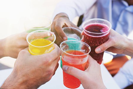 Téléchargez les photos : Détail sur les mains d'un groupe de jeunes tenant des boissons aux fruits carbonatés colorées dans des tasses en plastique, avec la lumière du soleil d'été filtrant à travers. - en image libre de droit