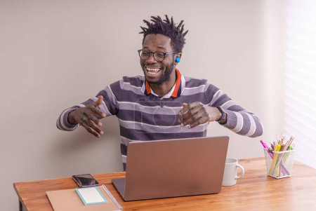 Foto de Estudiante afroamericano con peinado de cerraduras de arranque, con auriculares inalámbricos, involucrado en una videollamada en su computadora portátil, gesticulando mientras habla. - Imagen libre de derechos