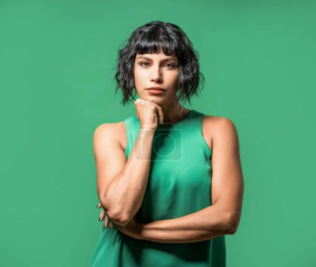 Photo for A striking brunette model, dressed in a green tank top, poses with her chin resting on her fist, giving a deep and serious look towards the camera. - Royalty Free Image