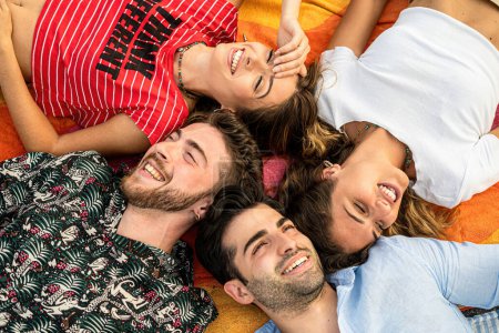 Téléchargez les photos : Quatre jeunes adultes, deux hommes et deux femmes, sont vus de haut en bas, couchés en cercle, souriant joyeusement à la caméra. - en image libre de droit