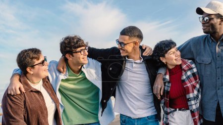 Téléchargez les photos : Un groupe multiracial joyeux de jeunes amis embrasse et rit ensemble à l'extérieur, profitant d'une belle journée de mi-saison, rayonnant d'unité et de bonheur. - en image libre de droit