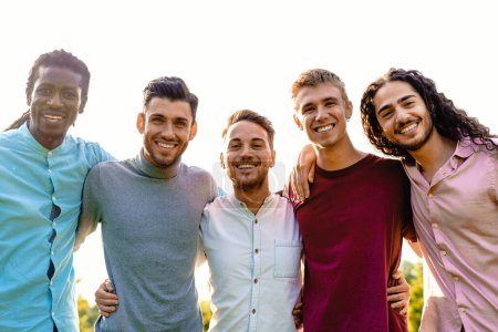 Téléchargez les photos : Un groupe multiracial de cinq amis masculins s'embrasse à l'extérieur, partageant un moment d'unité et de joie. Ils sourient tous chaleureusement, dirigeant leurs expressions joyeuses vers la caméra. - en image libre de droit