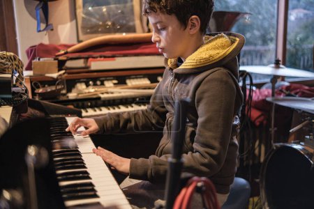 Téléchargez les photos : Un enfant de 10 ans montre son talent, jouant passionnément de l'orgue dans une salle de répétition, immergé dans le monde de la musique. - en image libre de droit
