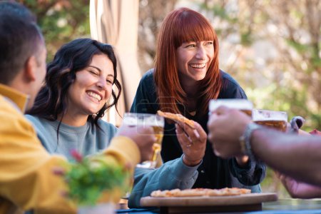 Foto de Un animado grupo de amigos saborea una comida informal al aire libre, sus risas y conversaciones creando recuerdos duraderos bajo el sol. - Imagen libre de derechos