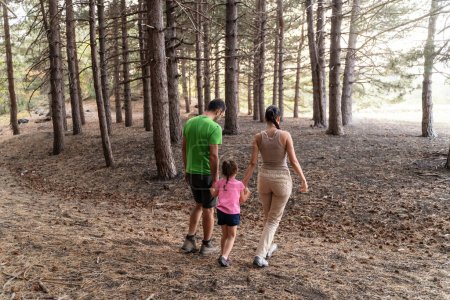 Téléchargez les photos : Aventure en forêt familiale - Une famille de trois personnes - un homme, une femme et une jeune fille - se promène dans une pinède. Le moment capte le lien et l'amour qu'ils partagent en explorant la nature ensemble. - en image libre de droit