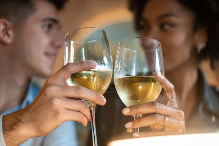 Photo for An intimate close-up of a young man and woman toasting with glasses of white wine. Their focused expressions and the clink of glasses symbolize celebration, connection, and shared happiness. - Royalty Free Image