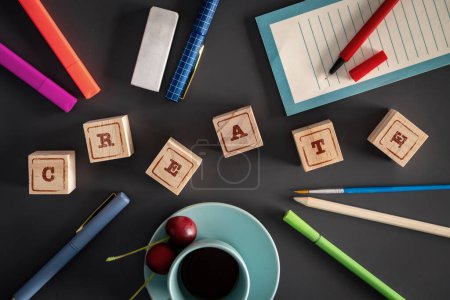 Flache Lage eines kreativen Schreibtischaufbaus mit "CREATE" in Holzklötzen, umgeben von Bastelmaterial und einer Tasse Kaffee.