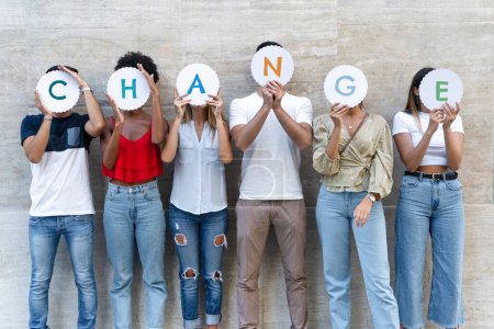 Eine Gruppe unterschiedlicher Individuen, die zusammenstehen und jeweils einen Buchstaben hochhalten, um gemeinsam das Wort "ÄNDERUNG" zu buchstabieren..