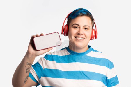 Téléchargez les photos : Enthousiaste androgyne individu portant des écouteurs et mettant en valeur un smartphone, représentant l'engagement technologique moderne. - en image libre de droit
