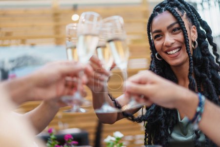 Téléchargez les photos : Une femme rayonnante avec des cheveux tressés griller avec des verres de champagne entre amis lors d'une célébration en plein air - Acclamations de groupe lors d'un rassemblement social. - en image libre de droit