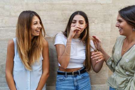 Téléchargez les photos : Trois jeunes femmes partagent un moment de légèreté, riant et appréciant la compagnie l'une de l'autre dans un cadre extérieur sincère. - en image libre de droit