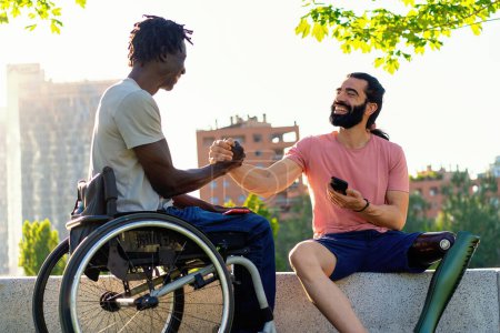 Photo for Two men, one with a prosthetic leg and one in a wheelchair, sharing a warm handshake in an urban outdoor setting. - Royalty Free Image