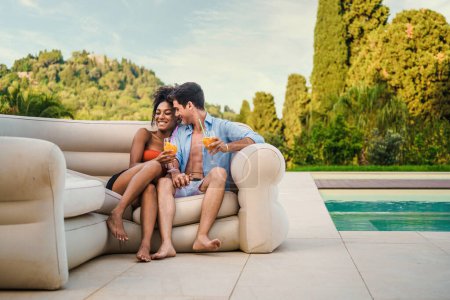 Téléchargez les photos : Couple partageant un moment romantique avec des boissons rafraîchissantes près de la piscine dans un cadre de villégiature luxueux. - en image libre de droit