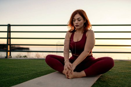 Foto de Mujer curvilínea practica yoga junto al mar, abrazando la serenidad y la atención plena durante una puesta de sol pacífica. - Imagen libre de derechos