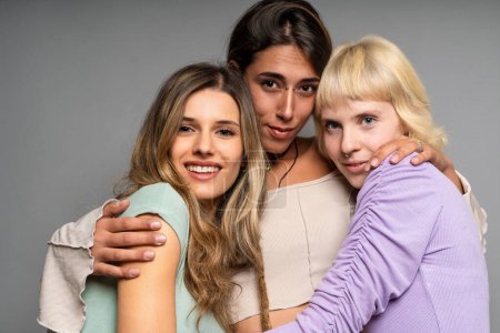 Photo for Three diverse women hugging and smiling in a studio setting, portraying warmth, friendship, and joyful connection. - Royalty Free Image