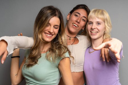 Photo for Three vibrant young women pointing and laughing together in a studio, sharing a playful and joyful connection. - Royalty Free Image