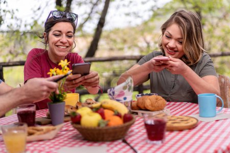 Téléchargez les photos : Deux femmes aiment capturer leur installation brunch dynamique sur smartphones, se livrant à la culture gastronomique. - en image libre de droit