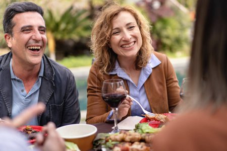 Foto de Dos amigos compartiendo una risa y vino durante una comida casual al aire libre, rodeados de naturaleza y una extensión de comida. - Imagen libre de derechos