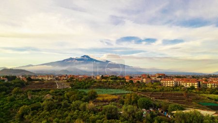 Foto de Vista aérea panorámica del Etna que se cierne sobre el exuberante paisaje y las zonas residenciales de Aci Sant 'Antonio, mostrando la grandeza del icónico volcán siciliano. - Imagen libre de derechos