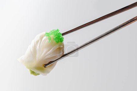 Photo for A pair of elegant chopsticks delicately grasps a translucent dumpling, topped with vibrant green caviar for a touch of luxury, isolated on a white background. - Royalty Free Image