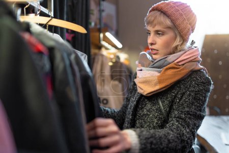 Téléchargez les photos : Une femme élégante parcourt les manteaux d'hiver dans une boutique, réfléchissant sur ses choix de mode. - en image libre de droit