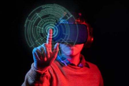 Jeune homme portant un casque VR avec des lumières bleues et rouges, appuyant sur un bouton virtuel à l'aide de la technologie de suivi à la main ; studio tourné sur fond noir.
