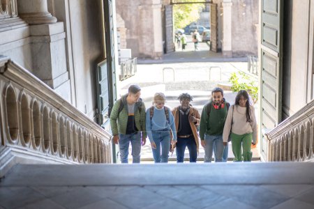 Téléchargez les photos : Groupe de jeunes adultes marchant occasionnellement dans un cadre urbain historique, incarnant l'exploration urbaine et l'amitié. - en image libre de droit