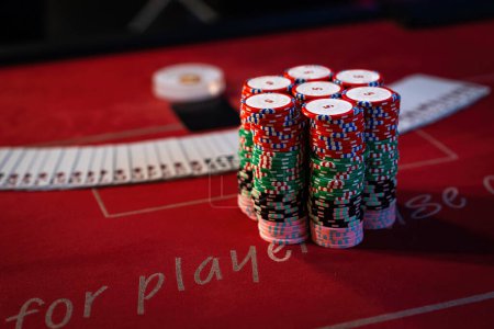Foto de Montones vívidos de fichas de póquer de colores y una extensión de cartas en una mesa de juego de casino rojo. - Imagen libre de derechos