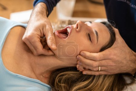 Photo for An osteopath performs a jaw adjustment on a female patient, focusing on alleviating tension and improving joint function. - Royalty Free Image