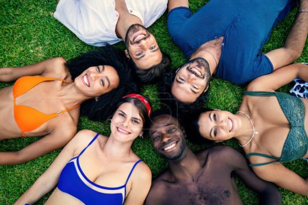 Diverse group of young friends in swimwear lying on grass, sharing a moment of joy and relaxation.