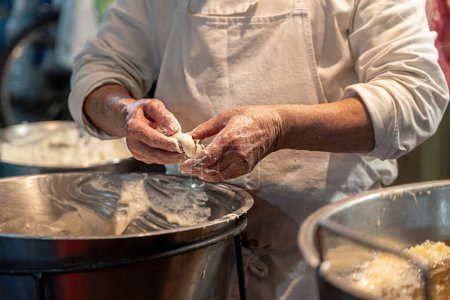 Chef bereitet sizilianische Crispelle auf einer Straße in Sizilien zu - Traditioneller frittierter Teig-Snack, der in lokaler Umgebung zubereitet wird.