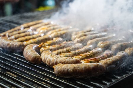 Photo for Close-up of sizzling sausages on a barbecue grill - Smoke rising from juicy grilled meat during an outdoor cookout. - Royalty Free Image