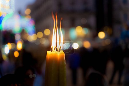 Téléchargez les photos : Une bougie brûle vivement contre un bokeh de lumières de la ville, symbolisant la foi et la tradition lors de la fête de Sainte Agathe à Catane - Lumière spirituelle aux chandelles dans la célébration culturelle - - en image libre de droit