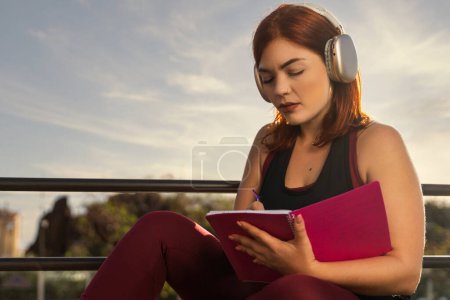 Concentrated female journaling outdoors - Inspiration through music - Serene environment for creativity.