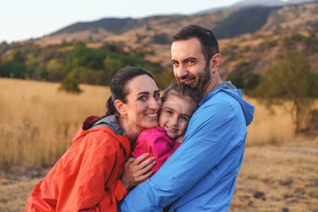 Téléchargez les photos : Gros plan d'une famille joyeuse embrassant la campagne lors d'une randonnée au coucher du soleil, partageant un moment chaleureux et aimant. - en image libre de droit
