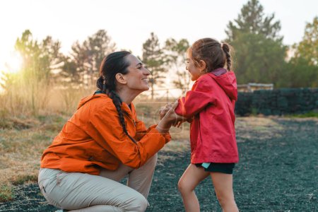 Téléchargez les photos : Mère et fille partagent un moment d'amour lors d'une randonnée au coucher du soleil, exprimant les liens familiaux dans la tranquillité de la nature. - en image libre de droit