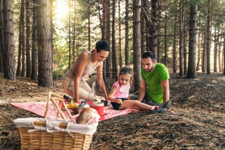 Family having a joyful picnic among trees, sharing food and smiles in a serene forest setting - family meal in woods - relaxing people lifestyle.