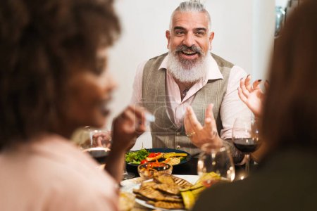Charismatic hipster man sharing stories with friends at dinner - Engagement and laughter over a meal in a warm indoor setting