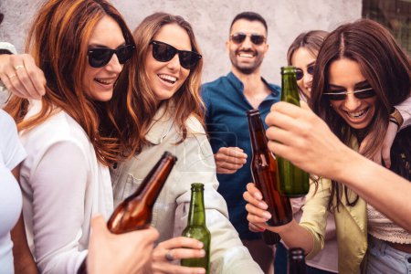 Téléchargez les photos : Un groupe dynamique d'amis griller avec des bières froides, lunettes de soleil sur fête en plein air joyeuse, moments de rire et acclamations, socialisation, mode de vie insouciant liens d'amitié, et de bons moments. - en image libre de droit