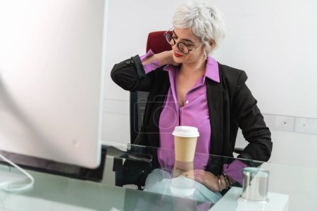 Foto de Mujer de negocios sénior que alivia la tensión en el cuello - fatiga en el trabajo, gestión del estrés en la oficina - Descanso de confort en horarios ocupados, Experiencia manejando presión. - Imagen libre de derechos