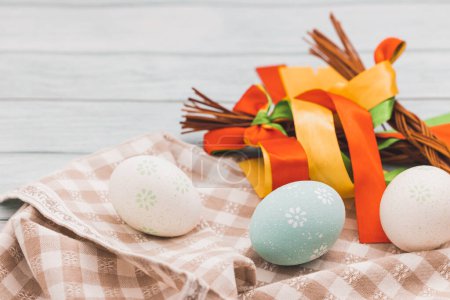 Easter decoration with painted eggs, colorful ribbons on a wooden table. Turquoise background
